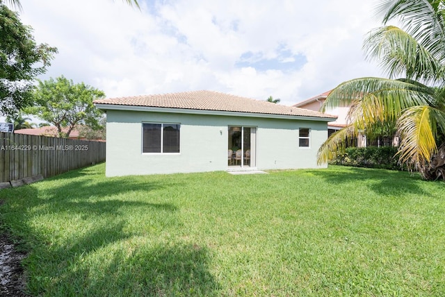 rear view of house featuring a fenced backyard, a lawn, a tiled roof, and stucco siding