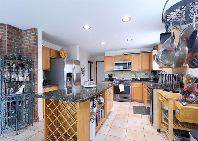 kitchen with stainless steel appliances, a kitchen island, tasteful backsplash, dark stone countertops, and light tile patterned floors