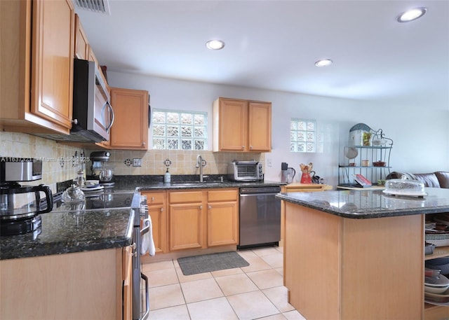 kitchen with sink, stainless steel appliances, light tile patterned floors, dark stone countertops, and a kitchen island