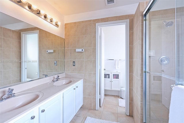 bathroom featuring tile patterned floors, vanity, a shower with door, and tile walls