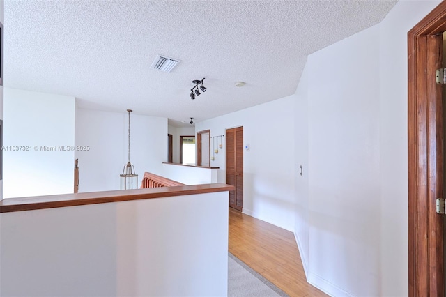 hall with a textured ceiling and light wood-type flooring