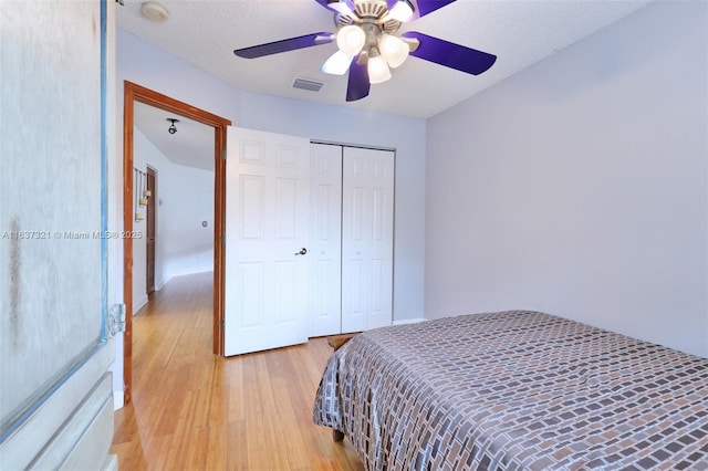 bedroom with ceiling fan, light hardwood / wood-style flooring, a textured ceiling, and a closet