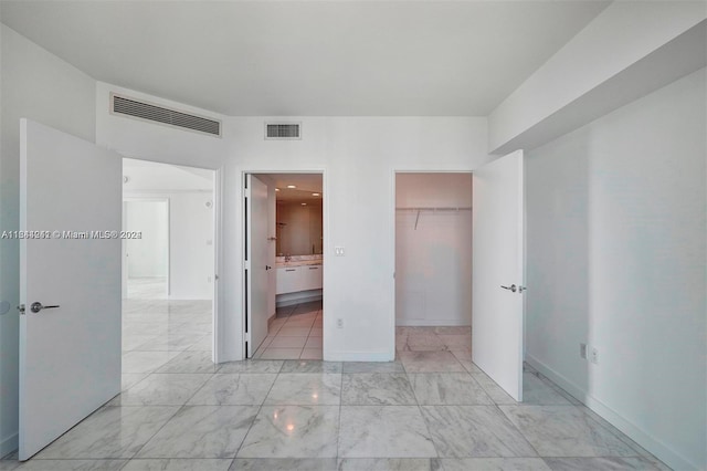 unfurnished bedroom featuring a spacious closet, a closet, ensuite bathroom, and light tile patterned flooring