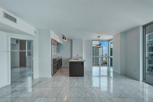 kitchen featuring light tile patterned flooring, expansive windows, built in fridge, pendant lighting, and a center island with sink