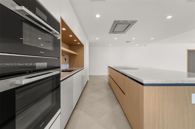 kitchen with sink, light stone counters, light tile patterned floors, black appliances, and white cabinets