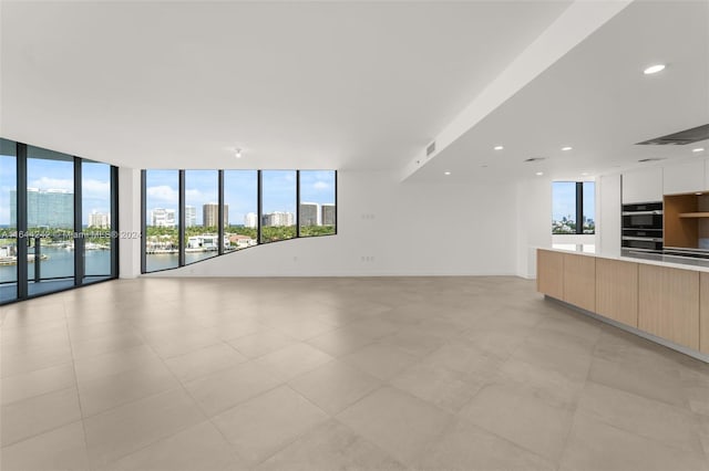 unfurnished living room with expansive windows, light tile patterned floors, and a water view