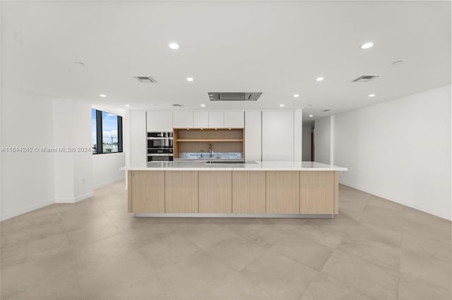 kitchen with light tile patterned floors, an island with sink, and white cabinets