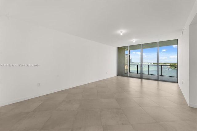 unfurnished room featuring light tile patterned floors, a wall of windows, and a water view