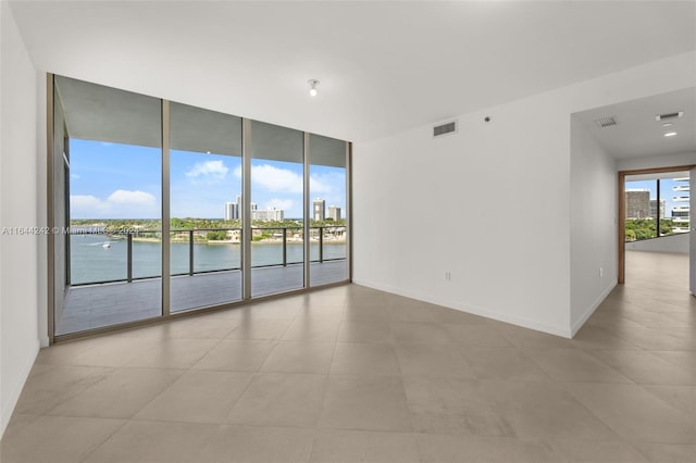 tiled empty room featuring expansive windows and a water view