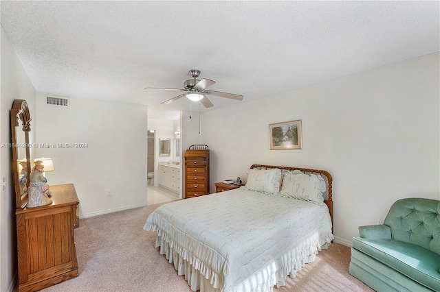 bedroom with ceiling fan, connected bathroom, a textured ceiling, and light carpet