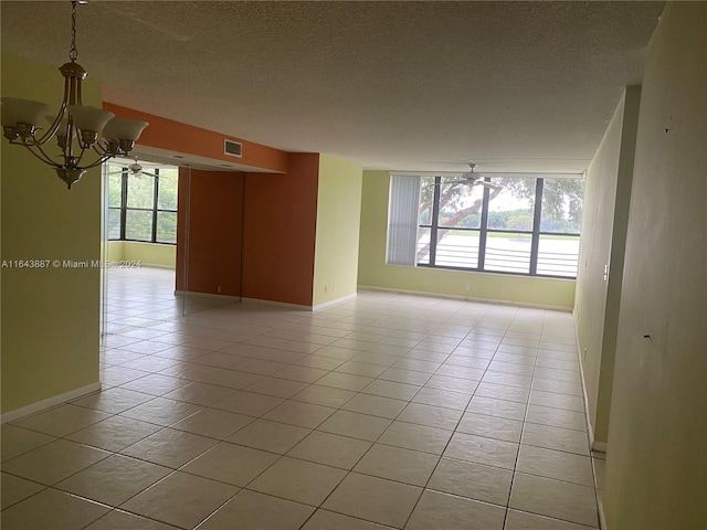 spare room with a wealth of natural light, tile patterned flooring, a textured ceiling, and an inviting chandelier