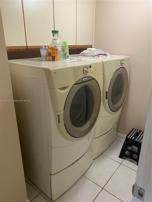 washroom featuring washing machine and dryer, light tile patterned flooring, and cabinets