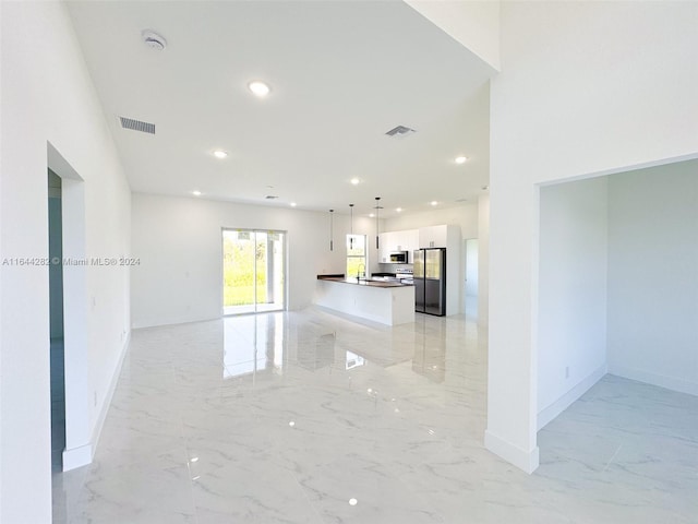 interior space featuring white cabinetry, appliances with stainless steel finishes, hanging light fixtures, and a center island