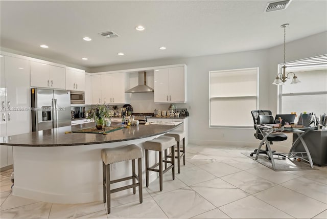 kitchen featuring a breakfast bar area, visible vents, stainless steel appliances, white cabinets, and wall chimney range hood