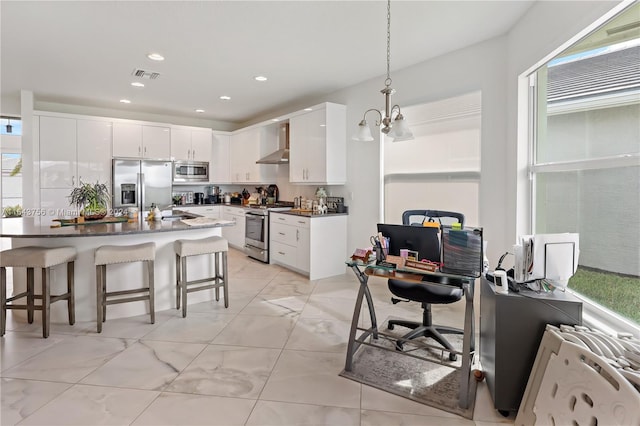 kitchen with visible vents, a breakfast bar, dark countertops, appliances with stainless steel finishes, and wall chimney range hood