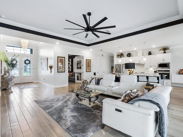 living room with crown molding, french doors, ceiling fan with notable chandelier, and light wood-type flooring