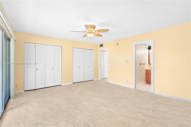 unfurnished bedroom featuring a textured ceiling, ensuite bathroom, ceiling fan, and two closets