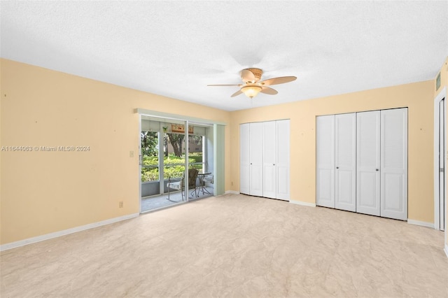 unfurnished bedroom with access to exterior, ceiling fan, light colored carpet, a textured ceiling, and two closets