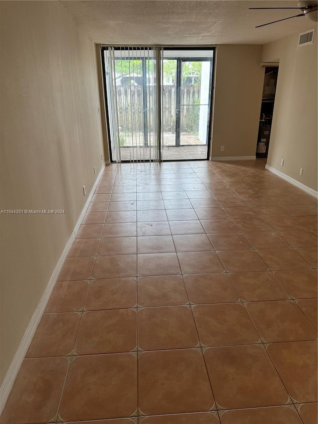 tiled spare room with visible vents, baseboards, ceiling fan, floor to ceiling windows, and a textured ceiling