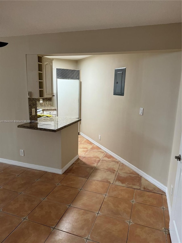 kitchen featuring built in refrigerator, electric panel, backsplash, a peninsula, and light tile patterned floors