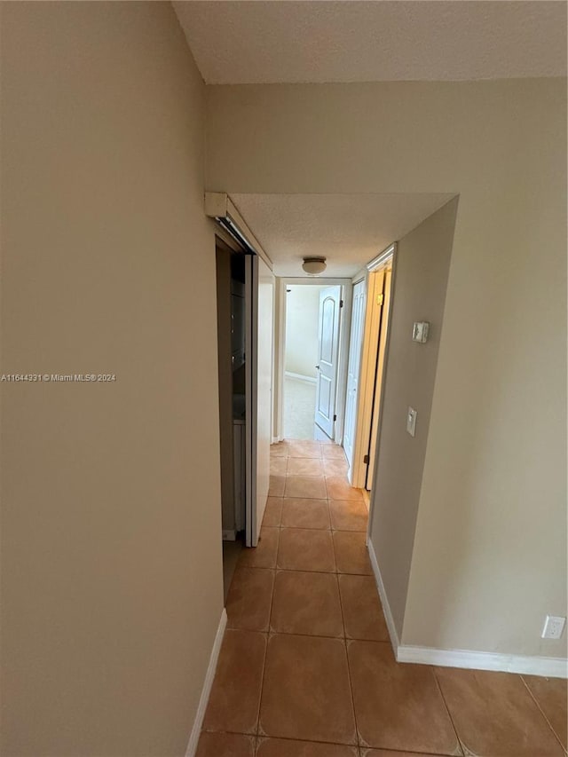 hallway featuring tile patterned flooring, a textured ceiling, and baseboards