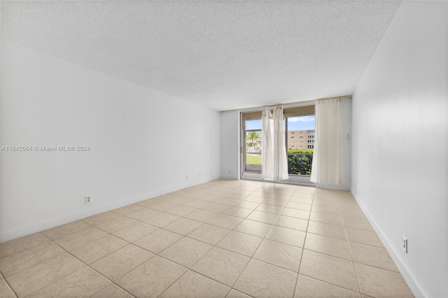 empty room featuring light tile patterned flooring, a wall of windows, and a textured ceiling