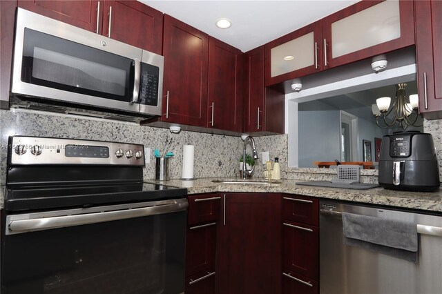 kitchen with tasteful backsplash, sink, a notable chandelier, light stone counters, and stainless steel appliances