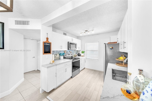 kitchen featuring appliances with stainless steel finishes, light stone counters, a textured ceiling, white cabinetry, and light tile patterned flooring