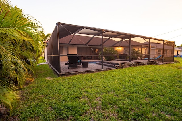 rear view of house featuring glass enclosure, a lawn, and a patio