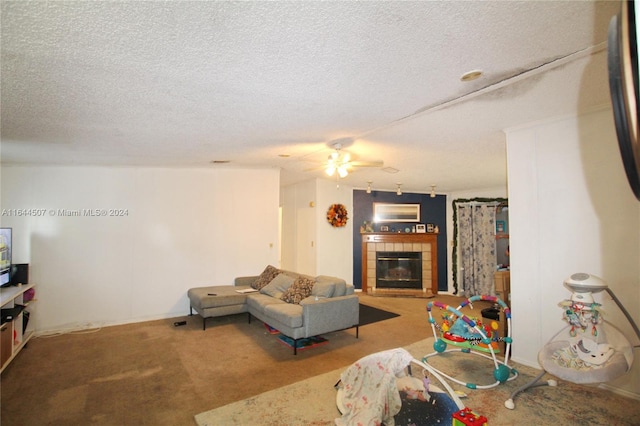 living room with ceiling fan, a tiled fireplace, a textured ceiling, and carpet floors