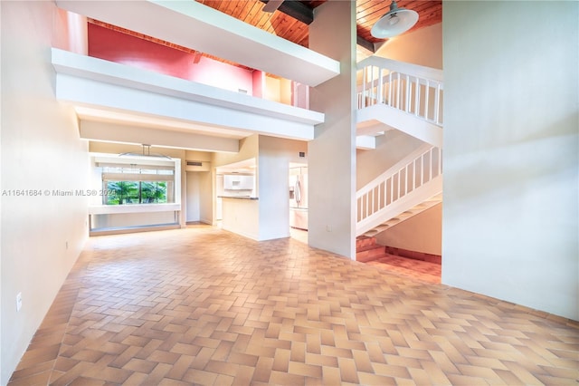 unfurnished living room featuring stairway, beamed ceiling, and a towering ceiling