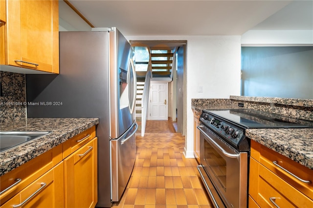 kitchen featuring stainless steel appliances, brown cabinetry, backsplash, and dark stone countertops