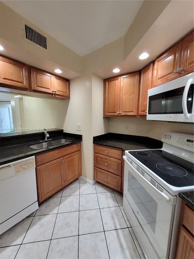 kitchen featuring sink, light tile patterned flooring, dark stone counters, and white appliances