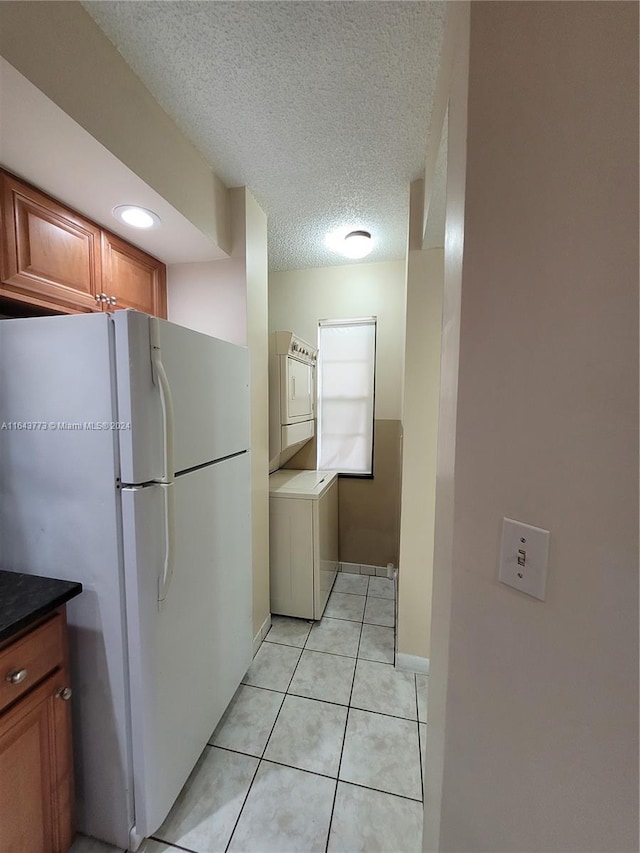 kitchen with a textured ceiling, white refrigerator, stacked washer and clothes dryer, and light tile patterned flooring