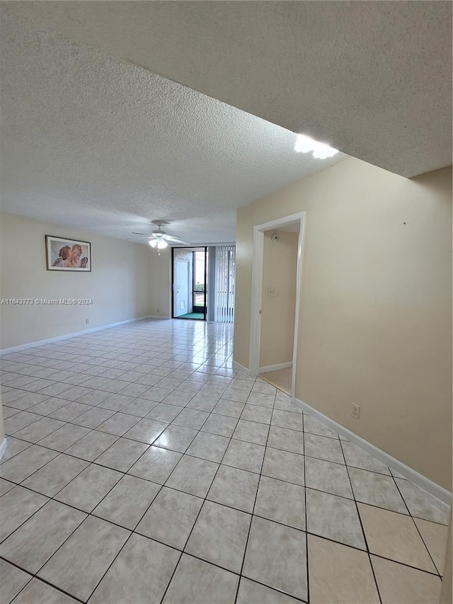 empty room with ceiling fan, light tile patterned floors, and a textured ceiling