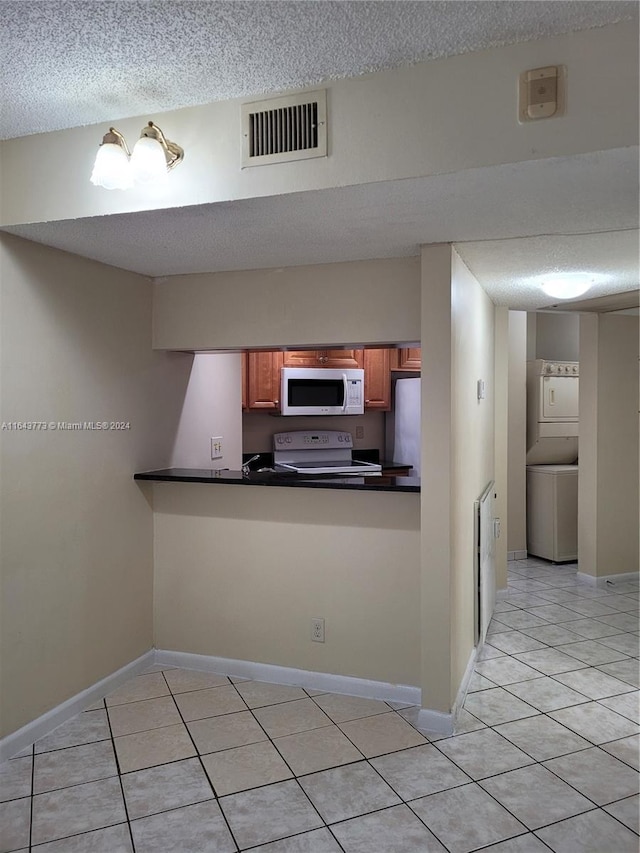 kitchen featuring kitchen peninsula, a textured ceiling, light tile patterned floors, stacked washer and clothes dryer, and range