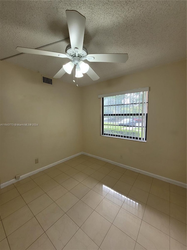 empty room featuring ceiling fan, light tile patterned flooring, and a textured ceiling