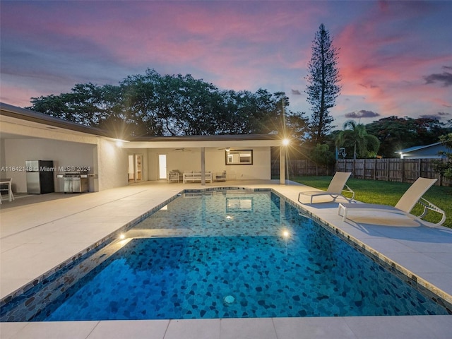 pool at dusk with a grill, a patio area, and a yard