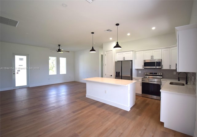 kitchen with a center island, white cabinets, hanging light fixtures, sink, and appliances with stainless steel finishes