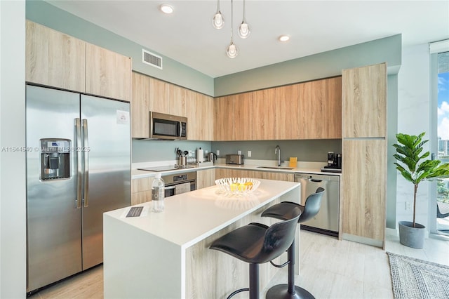 kitchen featuring a kitchen island, decorative light fixtures, sink, a breakfast bar area, and stainless steel appliances