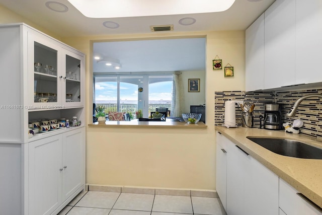 kitchen featuring decorative backsplash, white cabinetry, light stone counters, light tile patterned floors, and sink