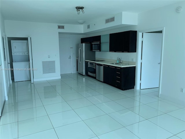 kitchen with stacked washing maching and dryer, stainless steel appliances, light tile patterned flooring, and sink