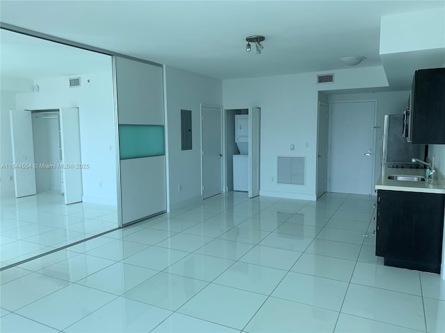 unfurnished living room with light tile patterned floors, electric panel, stacked washer and clothes dryer, and sink