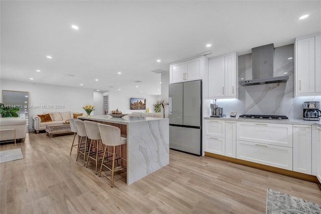 kitchen with wall chimney exhaust hood, appliances with stainless steel finishes, open floor plan, a kitchen bar, and white cabinetry