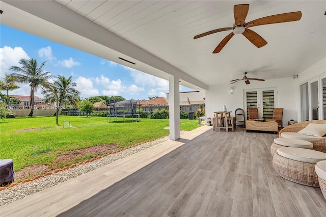 wooden terrace with ceiling fan, a patio, a trampoline, and a yard