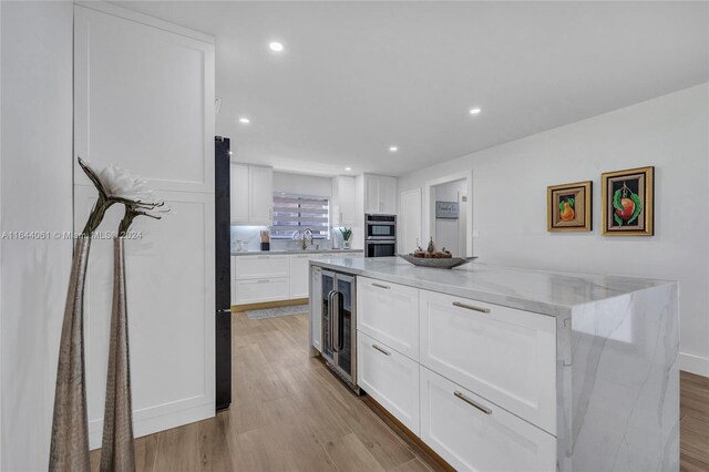 kitchen with white cabinetry, a center island, light hardwood / wood-style flooring, and light stone countertops