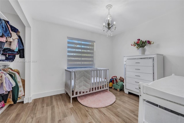 bedroom featuring a crib, light hardwood / wood-style flooring, and a chandelier