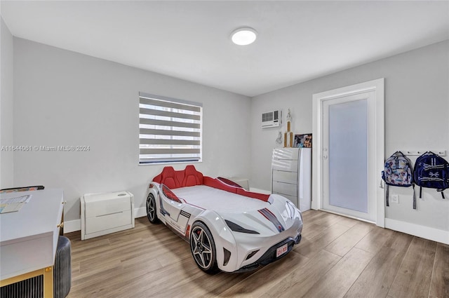 bedroom featuring an AC wall unit, wood finished floors, and baseboards