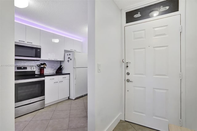 kitchen featuring tasteful backsplash, white cabinetry, a textured ceiling, light tile patterned flooring, and stainless steel appliances