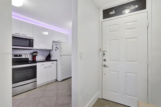 6219 Coral Lake Dr Unit 207, Margate, FL 33063 - kitchen with decorative backsplash, dark countertops, appliances with stainless steel finishes, white cabinetry, and light tile patterned floors